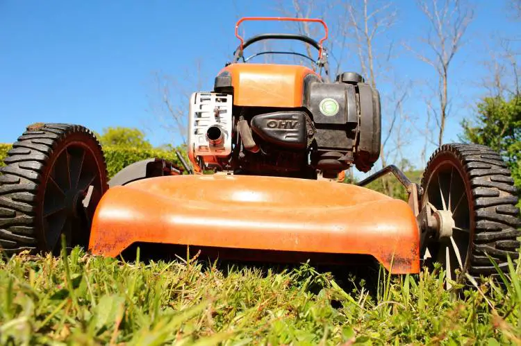 Close-up of an orange lawn mower on grass, with focus on blades and engine.
