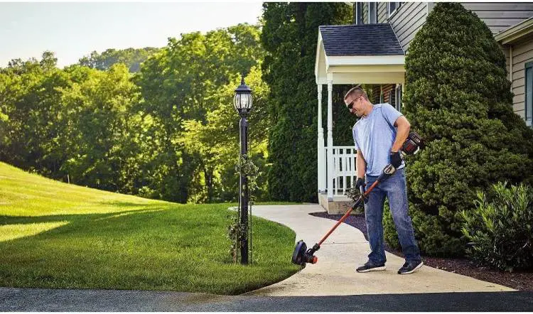 Man using a weed eater to trim edges of a manicured lawn.