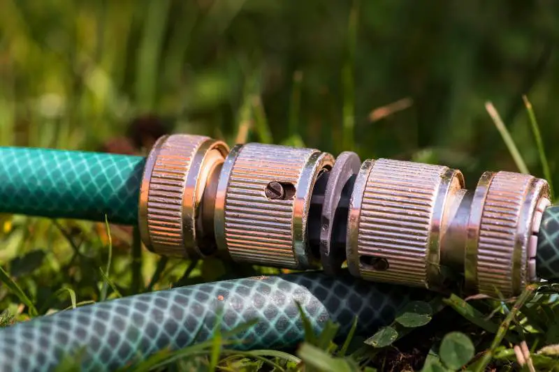 Close-up of a garden hose coupling with worn threads and signs of rust, lying on grass, hinting at potential failure points.