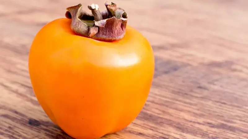 Single ripe persimmon fruit on a wooden surface, vibrant orange indicating the persimmon is ripe.