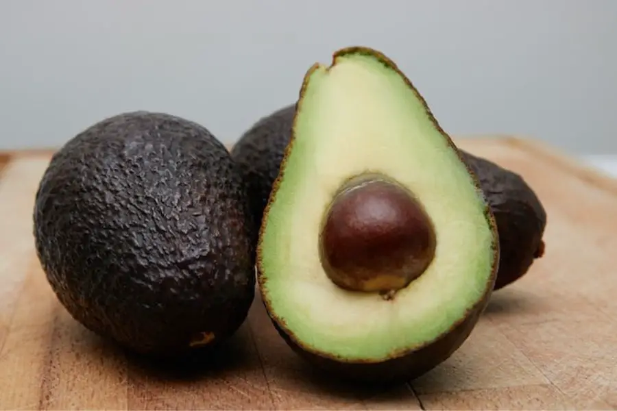 Ripe avocados, one halved to reveal a single large seed, on a wooden surface, exemplifying fruits with one seed.