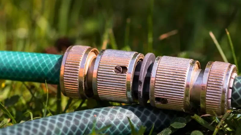 Why Does My Garden Hose Keep Bursting? - 8 Top Reasons 1 Close-up of a garden hose coupling with worn threads and signs of rust, lying on grass, hinting at potential failure points.