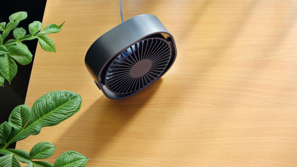Sleek black oscillating fan hanging over wood surface next to green plants.